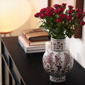 Ceramic vase with plum blossom floral pattern on console table with red roses