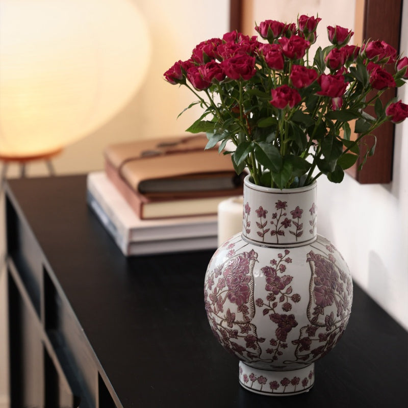 Ceramic vase with plum blossom floral pattern on console table with red roses