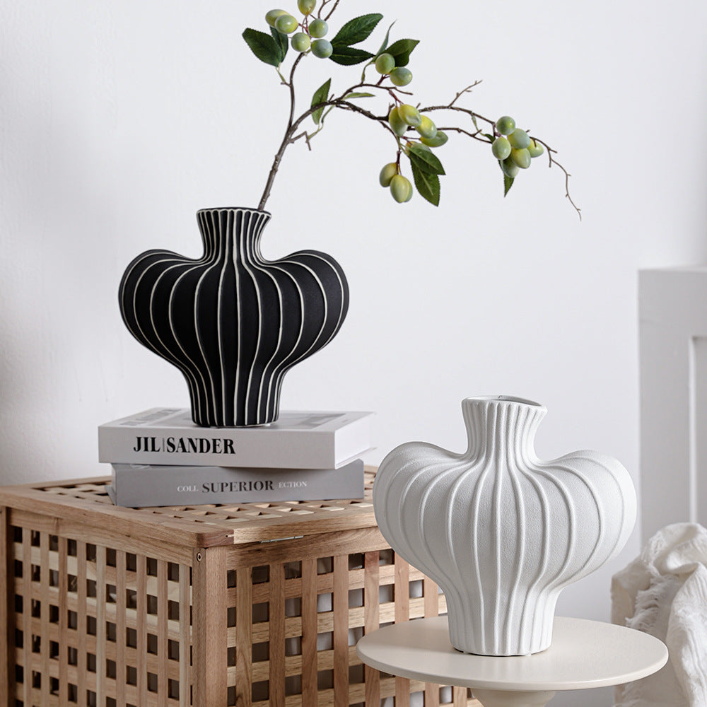 Black ceramic ribbed vase with green branches on wooden crate