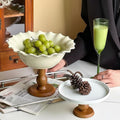 Scalloped white ceramic fruit bowl on wooden pedestal holding green grapes