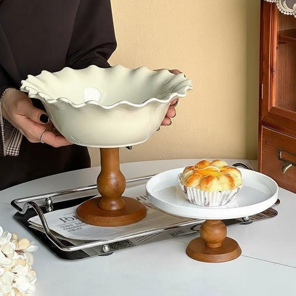 Hand holding white ceramic pedestal bowl next to small cake stand