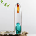 Clear art glass cylindrical sculpture with amber and teal accents standing on tray
