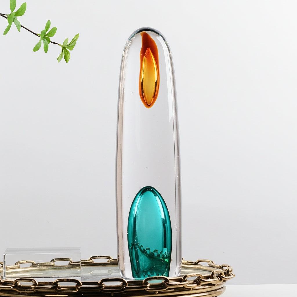 Clear art glass cylindrical sculpture with amber and teal accents standing on tray