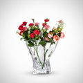 Clear crystal sculptural vase holding pink and red flowers on a white background