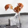 Clear glass vase melting over grey marble cube with dried flowers