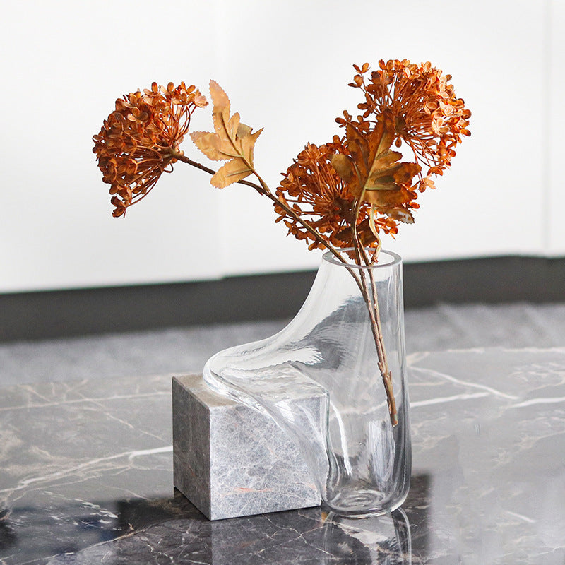 Clear glass vase melting over grey marble cube with dried flowers