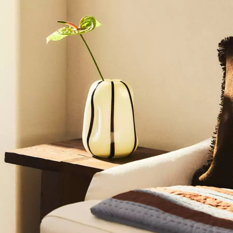 Organic cream and black striped glass vase with green flower on wooden table