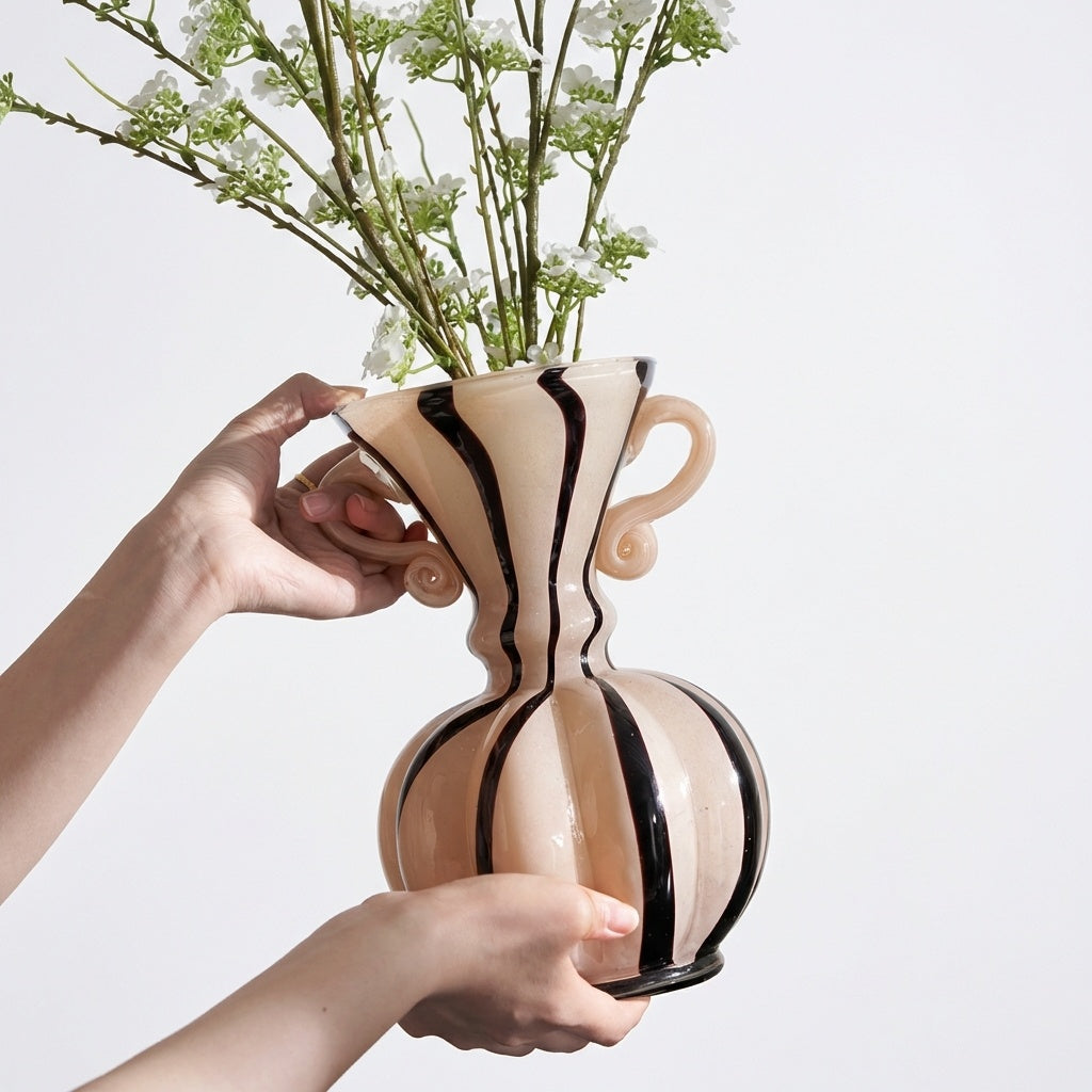 Hands holding the cream and black striped glass vase