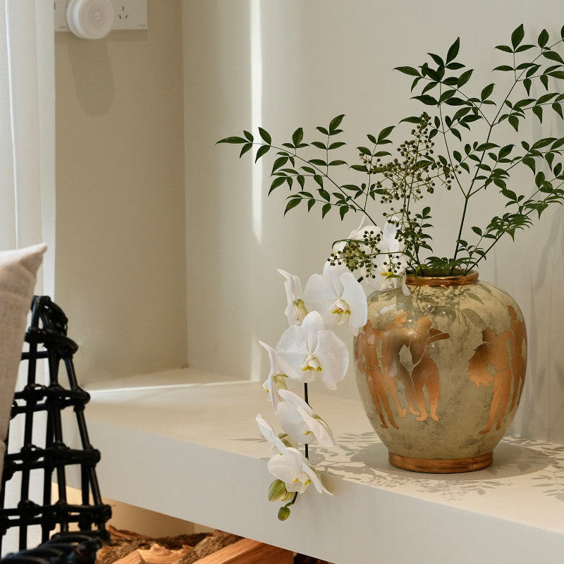 Detail of gold figures on ceramic vase with white orchids