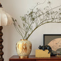 Ceramic vase with gold Grecian motif on wooden sideboard