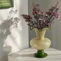 Cream and green glass ruffled vase casting shadows against a white wall