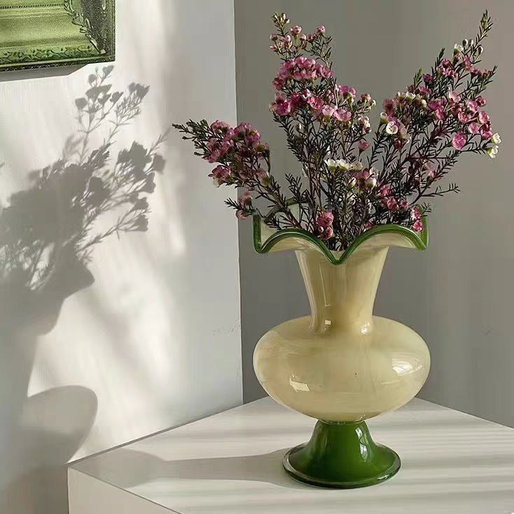 Cream and green glass ruffled vase casting shadows against a white wall