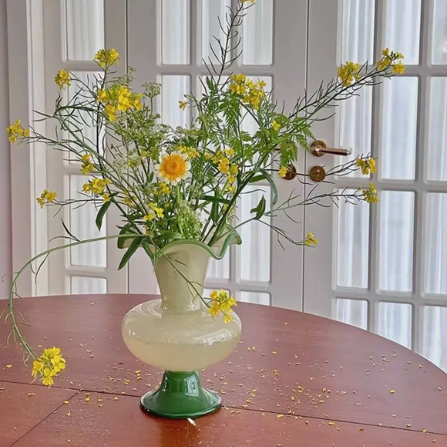 Glass pedestal vase filled with yellow wildflowers on a wooden table