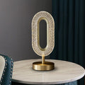 Front view of illuminated crystal acrylic and brass oval table lamp