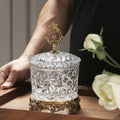 Close up of cut glass jar with brass lid handle and base held by hand