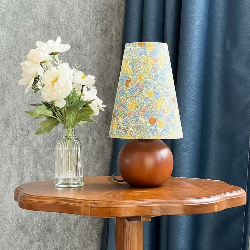 Side view of floral table lamp on wooden side table next to flowers