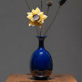 Deep blue glazed ceramic bottle vase with dried flowers on wooden table