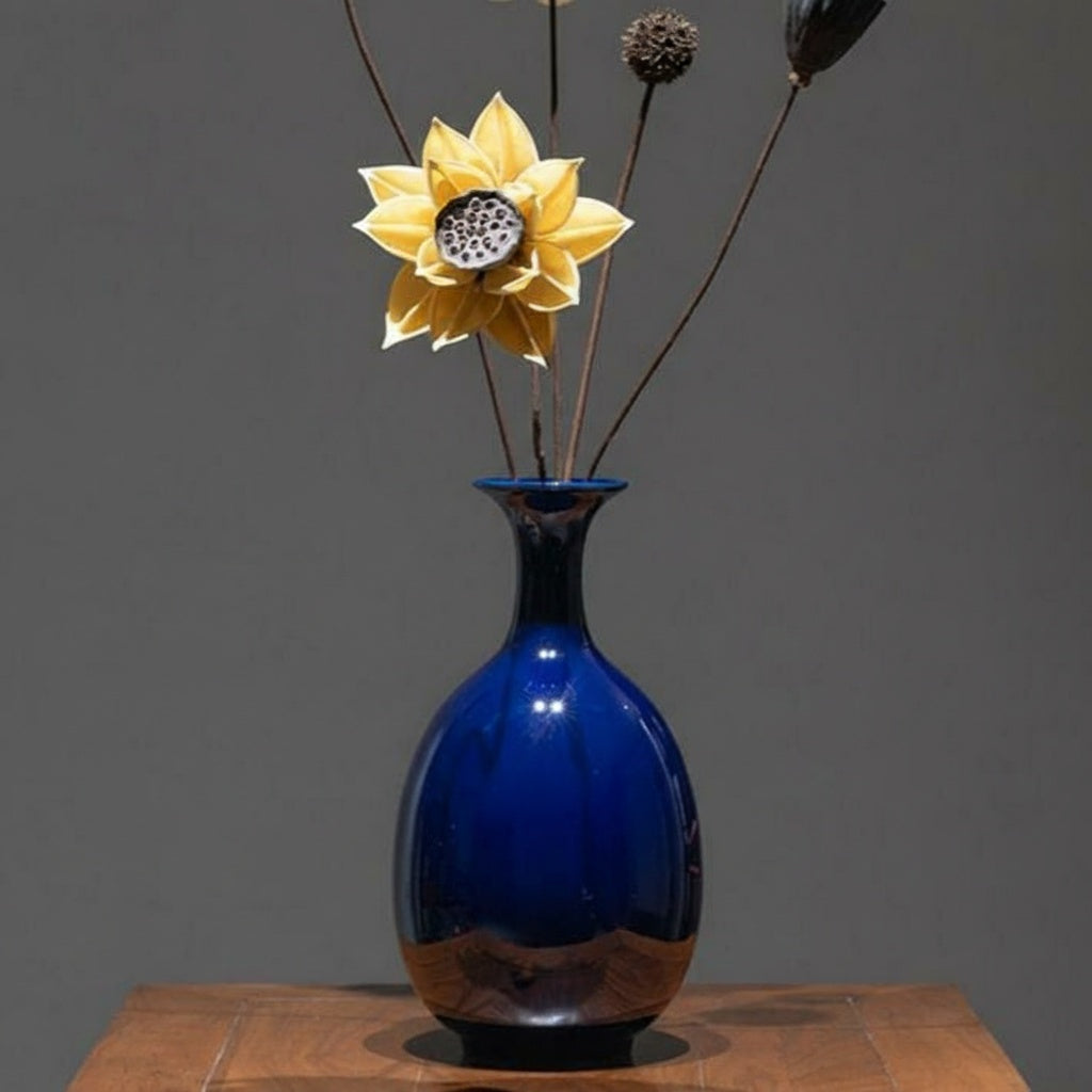 Deep blue glazed ceramic bottle vase with dried flowers on wooden table