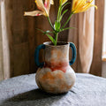 Distressed ceramic amphora vase with blue handles and lilies