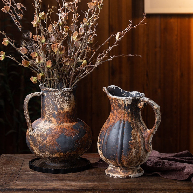 Two distressed ceramic pitcher vases with dried flowers on a wooden table