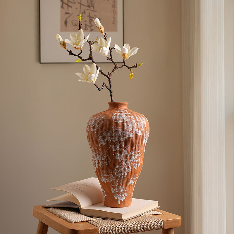 Side view of rustic orange and white ceramic vase on woven stool