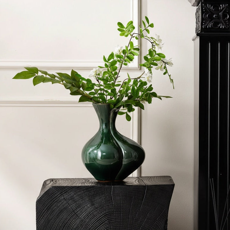 Glossy emerald vase with greenery on dark wood pedestal