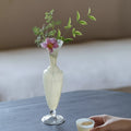Frosted glass pedestal vase with pink flower on a table