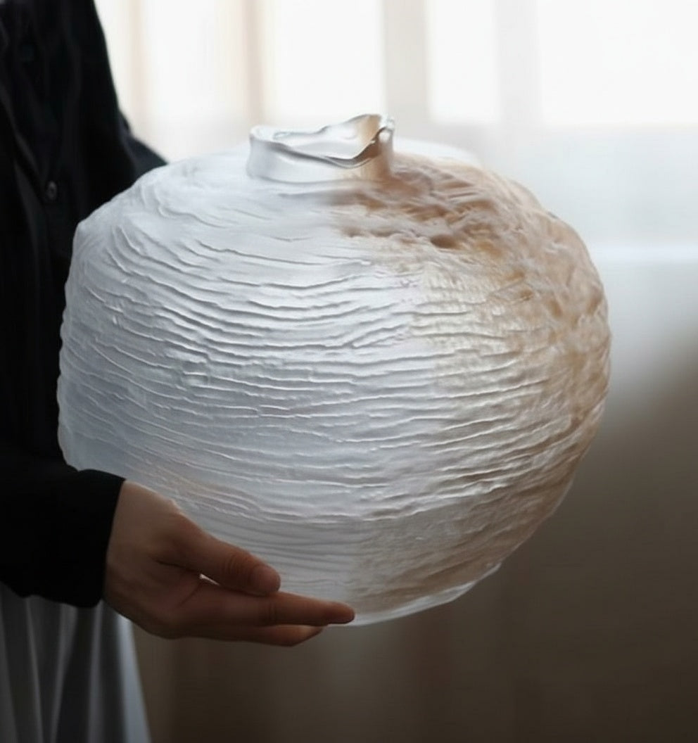 Side view of heavy textured white glass vase held in hands