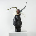Black faceted resin vase with eucalyptus stems on white pedestal