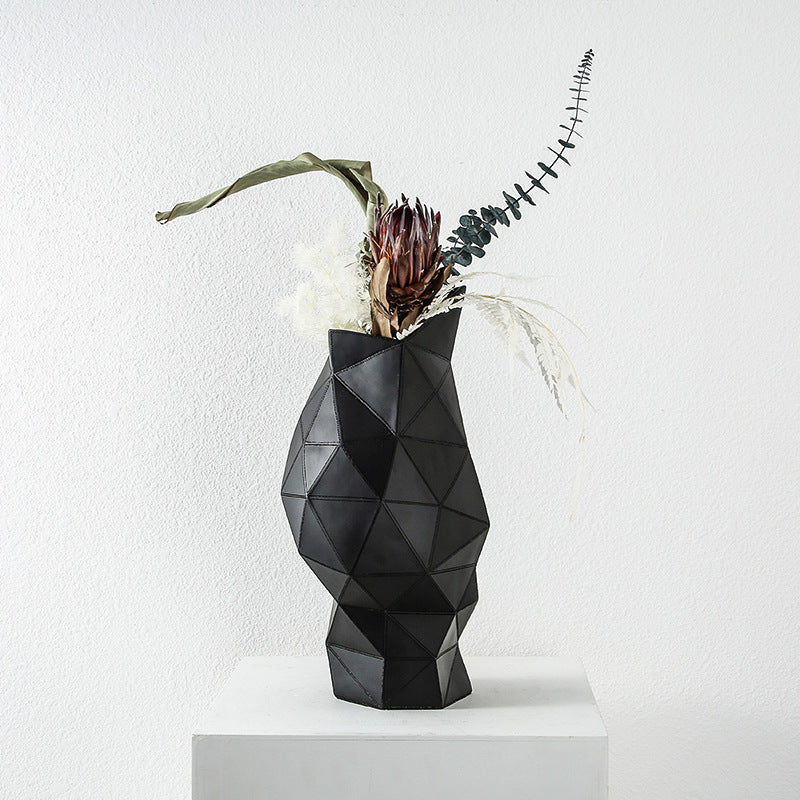 Black faceted resin vase with eucalyptus stems on white pedestal