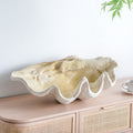 Oversized resin clam shell decorative bowl styled on a light wood cabinet in a neutral interior