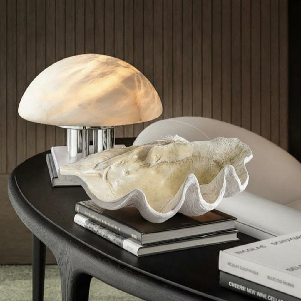 Large beige resin clam shell bowl styled on a black side table with lamp and books