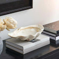 Large resin clam shell decorative bowl styled on stacked books in a modern interior