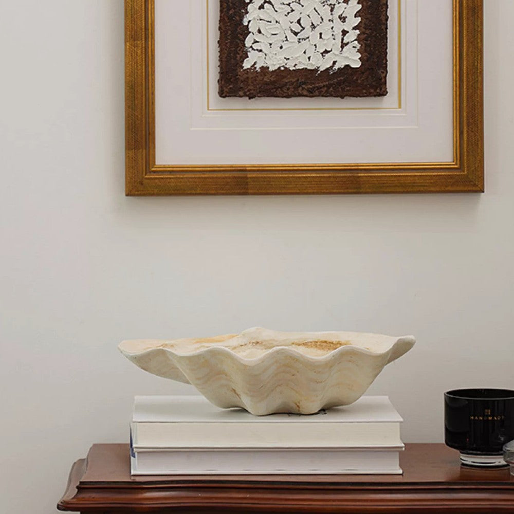 Large resin clam shell decorative bowl on stacked books against framed wall art