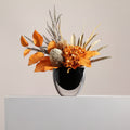 Front view of black glass vase with orange dried flowers