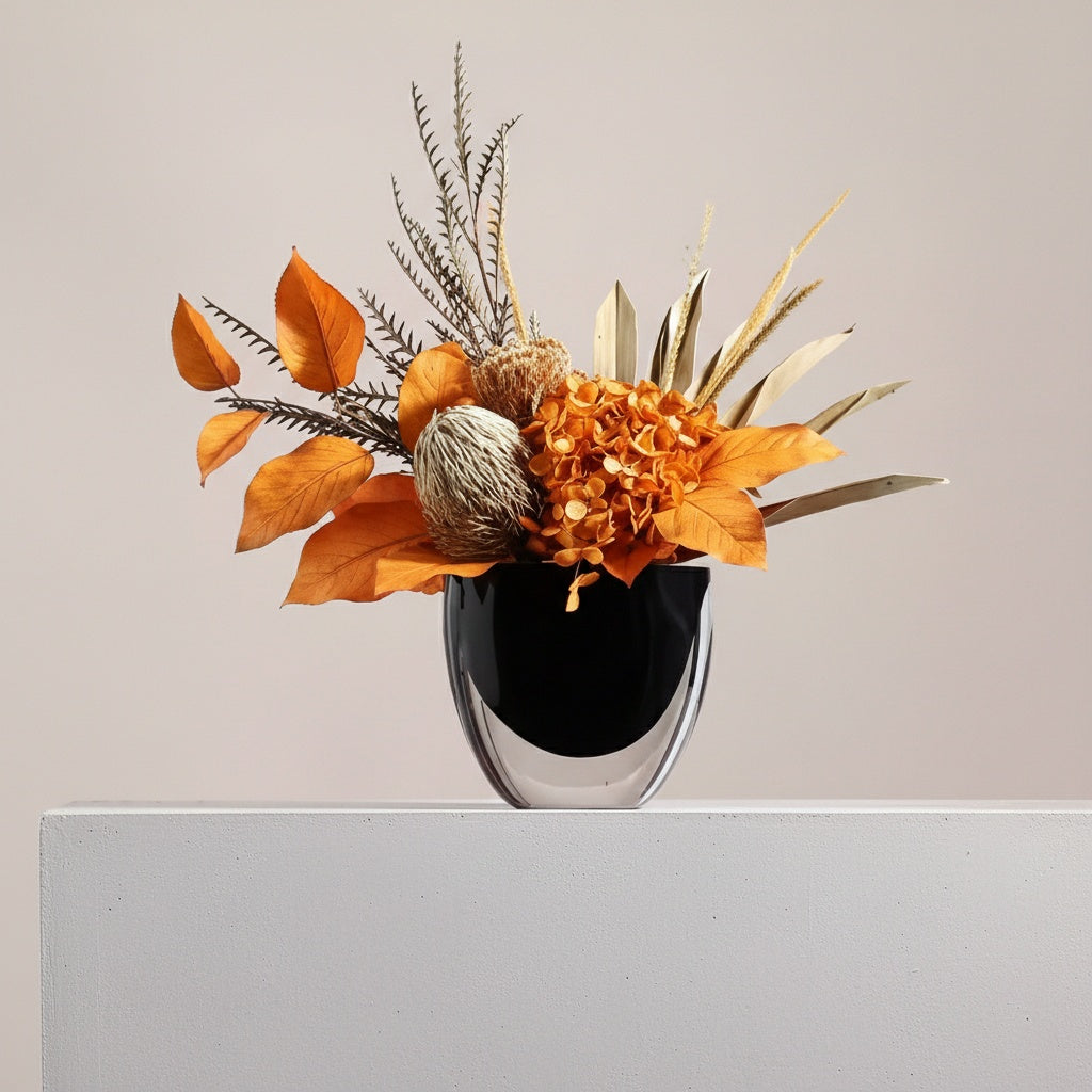 Front view of black glass vase with orange dried flowers