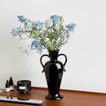 Glossy black ceramic vase with blue flowers on wooden table