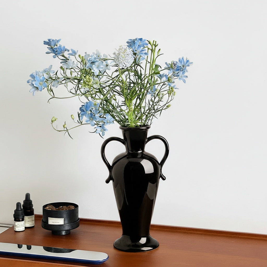 Glossy black ceramic vase with blue flowers on wooden table