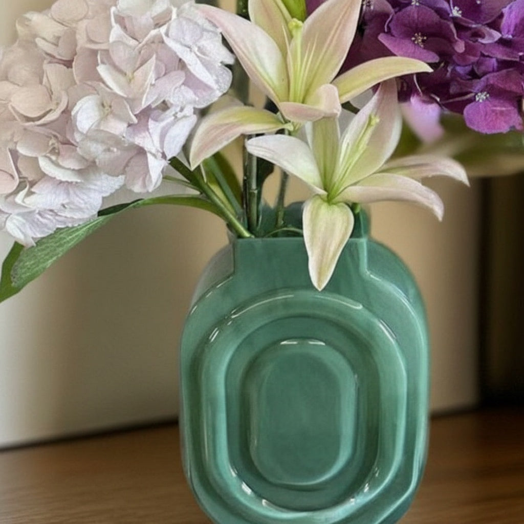 Glossy green oval vase holding white and purple flowers