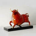 Angled front view of red and gold bull statue on black base