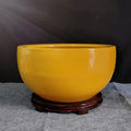 Glossy yellow ceramic decorative bowl on wooden stand