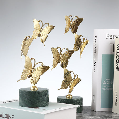 Handcrafted copper butterfly sculptures on green marble stands displayed on a marble table with books