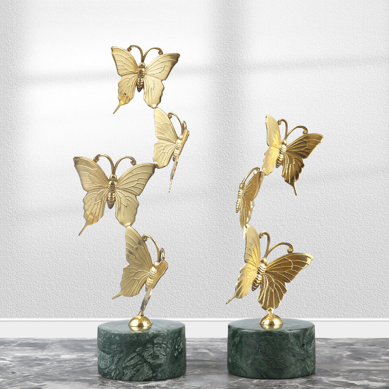 Two sizes of gold copper butterfly sculptures with green marble bases standing side by side