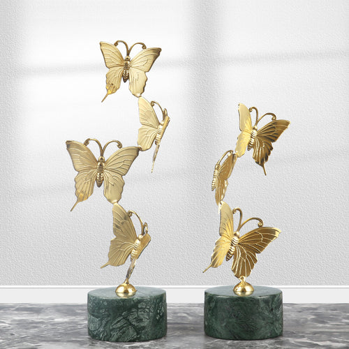 Two sizes of gold copper butterfly sculptures with green marble bases standing side by side