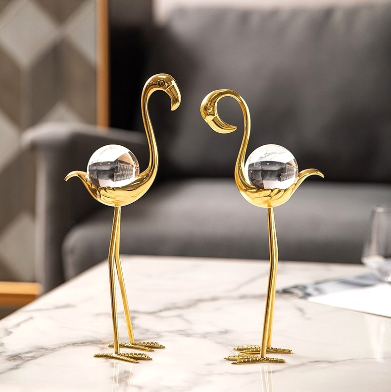 Front view of two gold and crystal flamingo figurines on a table