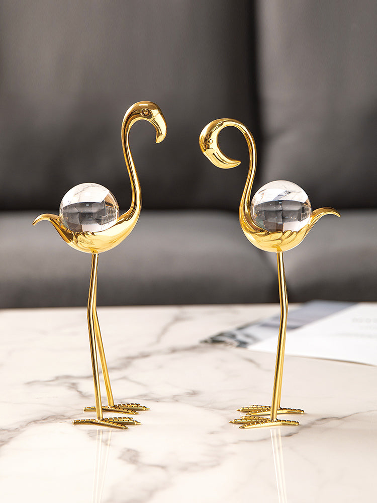 Two gold flamingo figurines with crystal bodies on a marble table
