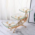 Angled view of gold and glass 3-tier serving stand with floral details