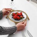 Ornate gold and glass footed serving tray held by hands with fruit