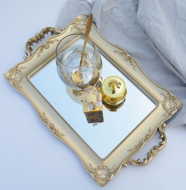 Overhead view of gold baroque serving tray holding a glass cup and perfume bottle