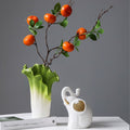 Gradient green and white ceramic vase with ruffled leaf rim holding decorative branches